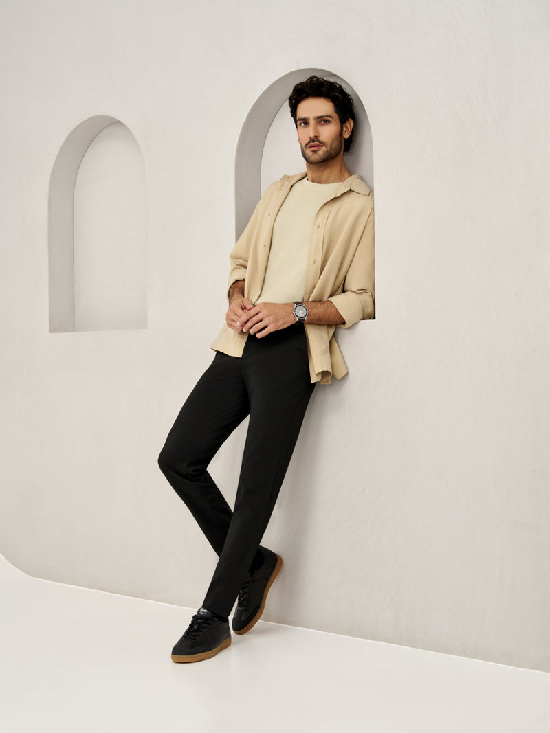 A man standing against an arched wall, wearing bangalore black pants from the Pant Project