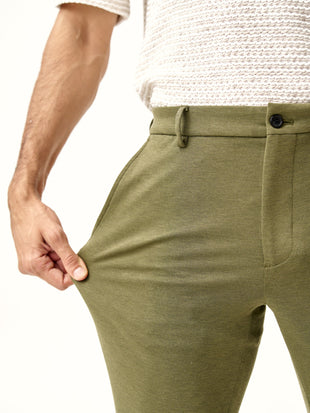 hand stretching the military green custom pants fabric, showcasing flexibility, the Pant Project