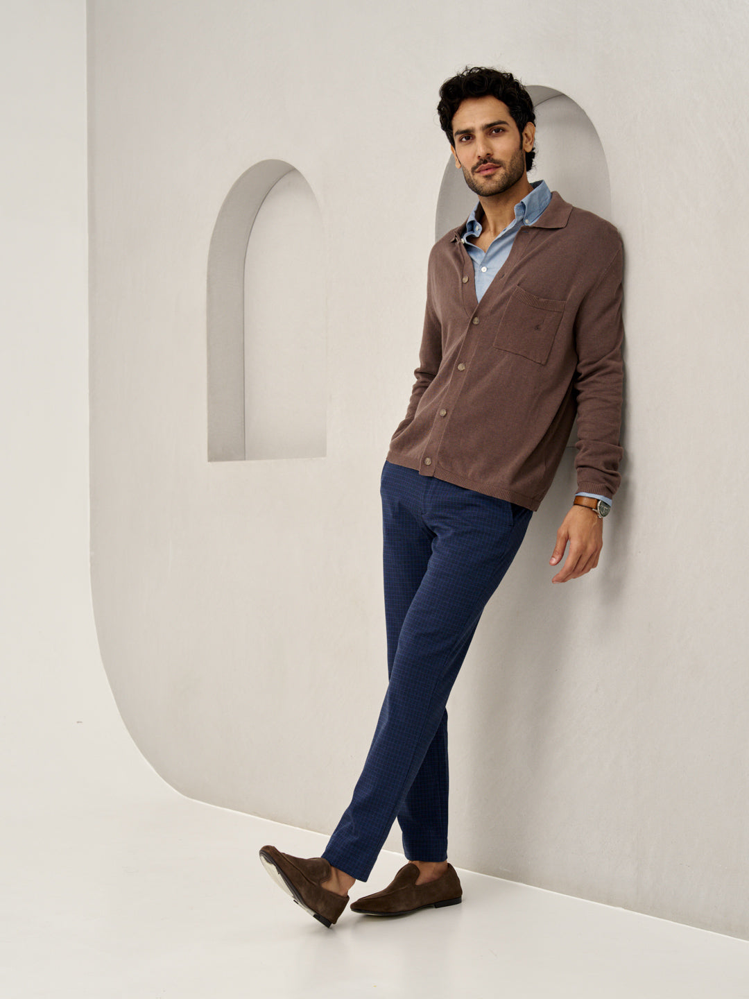 man leaning against wall, wearing blue check pants and brown cardigan from the Pant Project