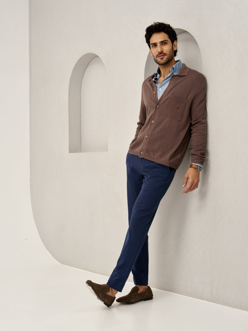 man leaning against wall, wearing blue check pants and brown cardigan from the Pant Project
