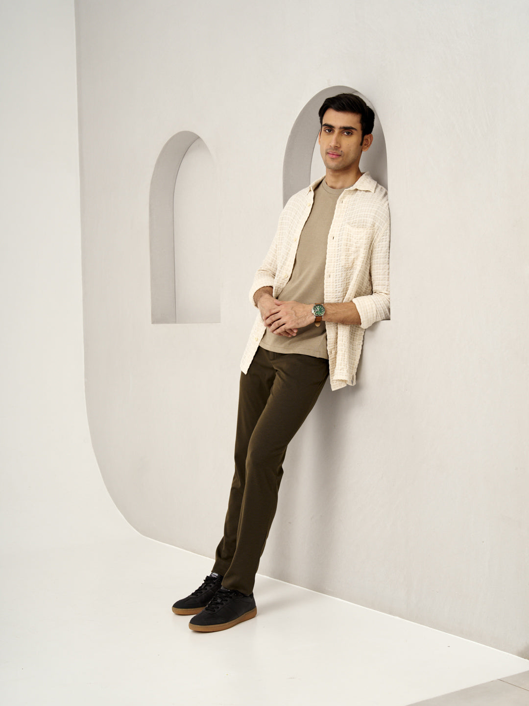 relaxed model posing against a wall, wearing martini olive pants by the Pant Project