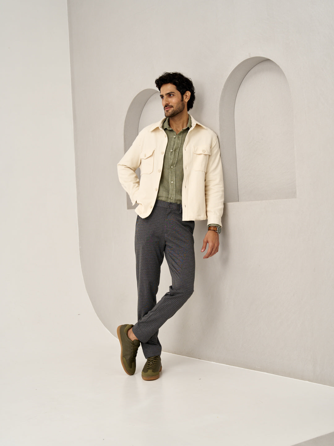 stylish man leans against a wall wearing grey check pants by the Pant Project
